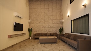 A living room with a stone wall, a flat-screen TV, a sofa, a coffee table, and two potted plants. - Dornix by Housiify (Gurugram)