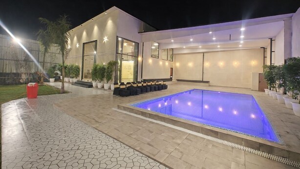 A modern building with a large outdoor swimming pool, a covered seating area, and potted plants. - Dornix by Housiify (Gurugram)