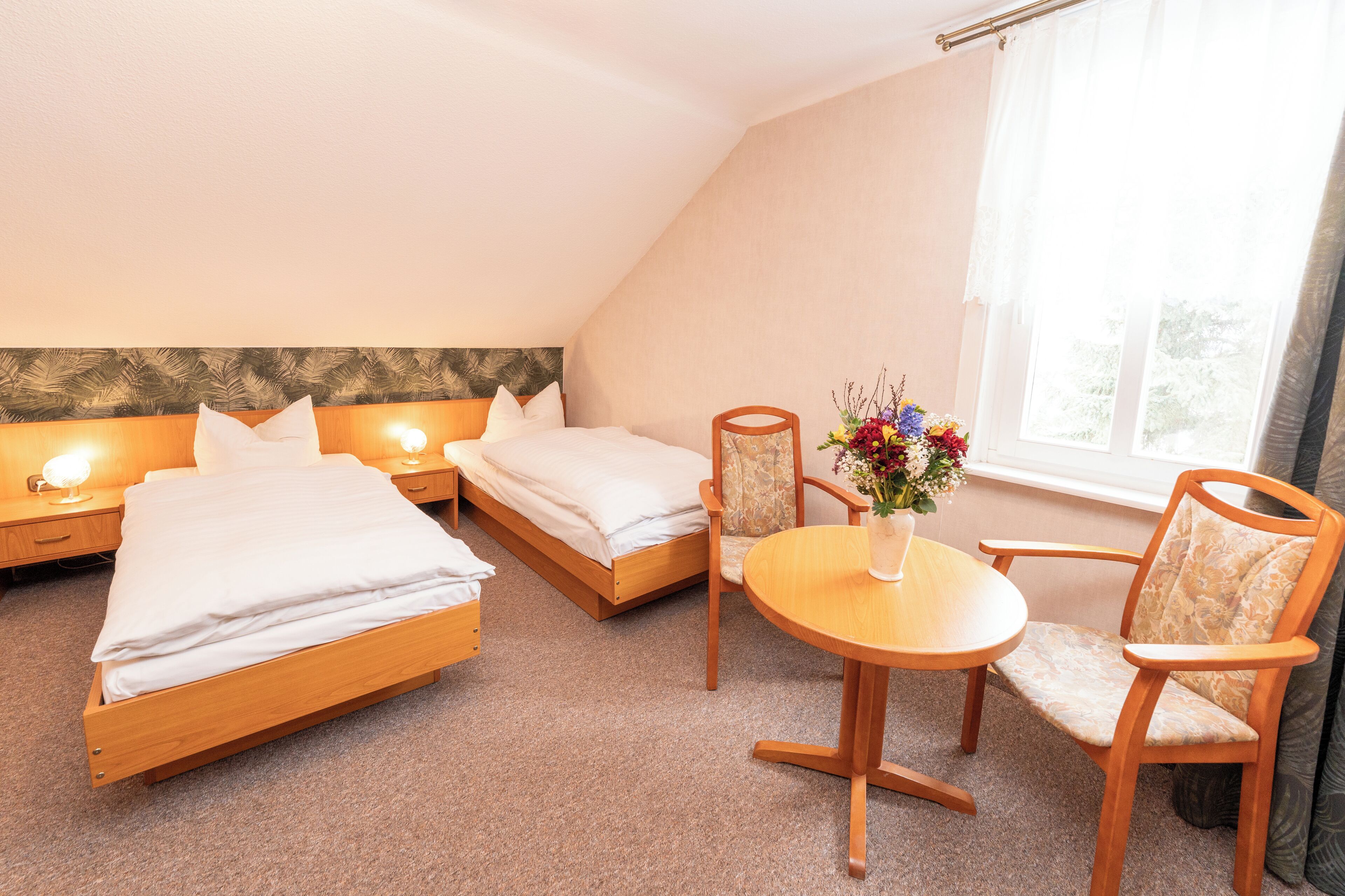 Et hotelværelse med to enkeltsenge, et lille rundt bord med en vase blomster og en stol.