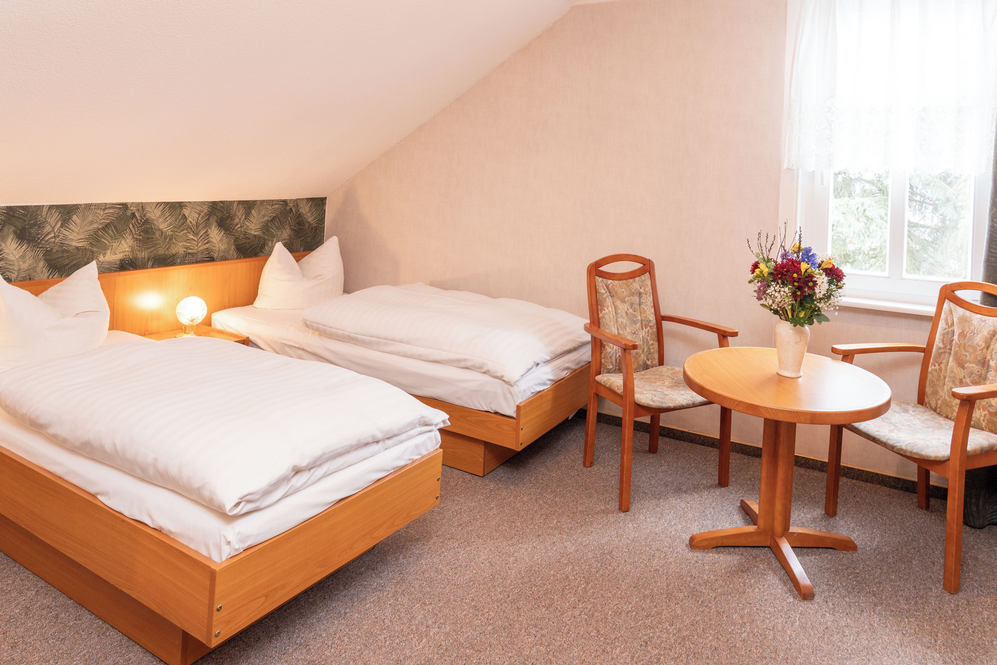 Ein Schlafzimmer mit zwei Betten, einem Holz-Kopfteil, einem kleinen runden Tisch mit Stühlen und einem Fenster mit Vorhängen.