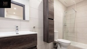 A modern bathroom with a white sink, dark wood vanity, a glass shower enclosure, and a white toilet. - A lovely vacation 5BR/5BATH home with WIFI & AC (L-Imsida)