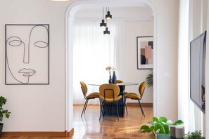 Un espace repas moderne avec une table ronde et des chaises jaunes, des œuvres d’art encadrées accrochées aux murs et un plancher en bois.