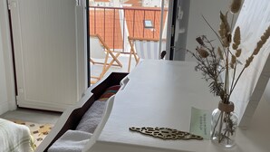 Una habitación con una cama, una mesita con un florero y vistas a edificios a través de una ventana.