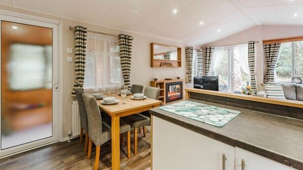 A modern kitchen with a dining area, a built-in oven, and a large window with curtains. - Sea Squirrel - Kelling Heath Holiday Park - 15856 (Holt)