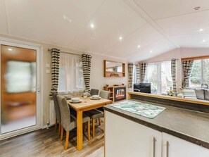 A modern kitchen with a dining area, a built-in oven, and a large window with curtains. - Sea Squirrel - Kelling Heath Holiday Park - 15856 (Holt)