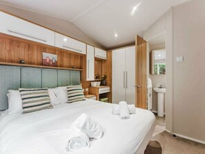 Ein modernes Hotelzimmer mit einem großen Bett, einem Holzkopfteil, einem Schminktisch mit Spiegel und einem Kleiderschrank.