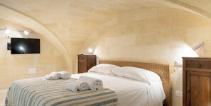 A hotel room with a bed, a flat-screen TV mounted on the wall, and a wooden nightstand. - Hotiday Torre Guaceto (Brindisi)
