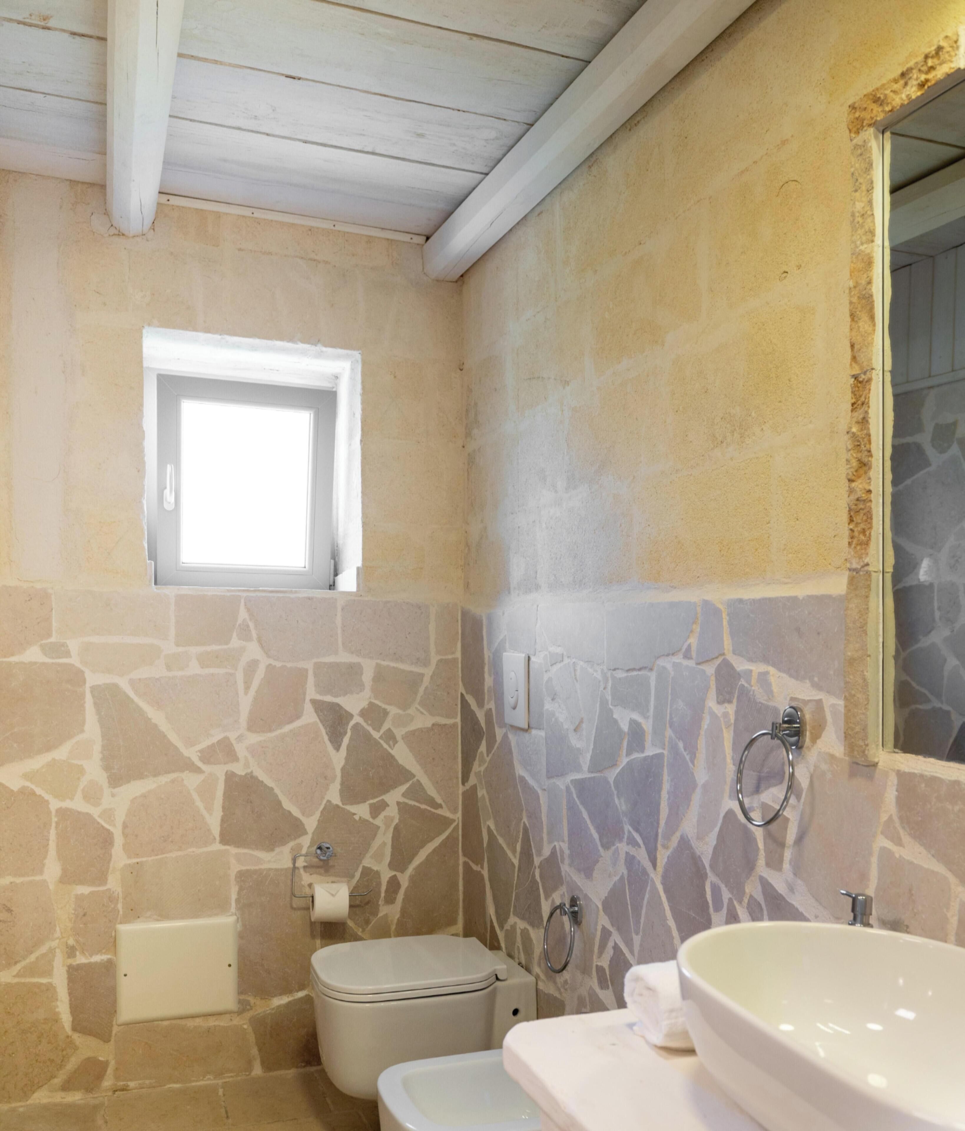 Un baño con paredes de piedra, una ventana, un inodoro y un lavabo.