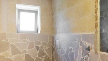 Un baño con paredes de piedra, una ventana, un inodoro y un lavabo.