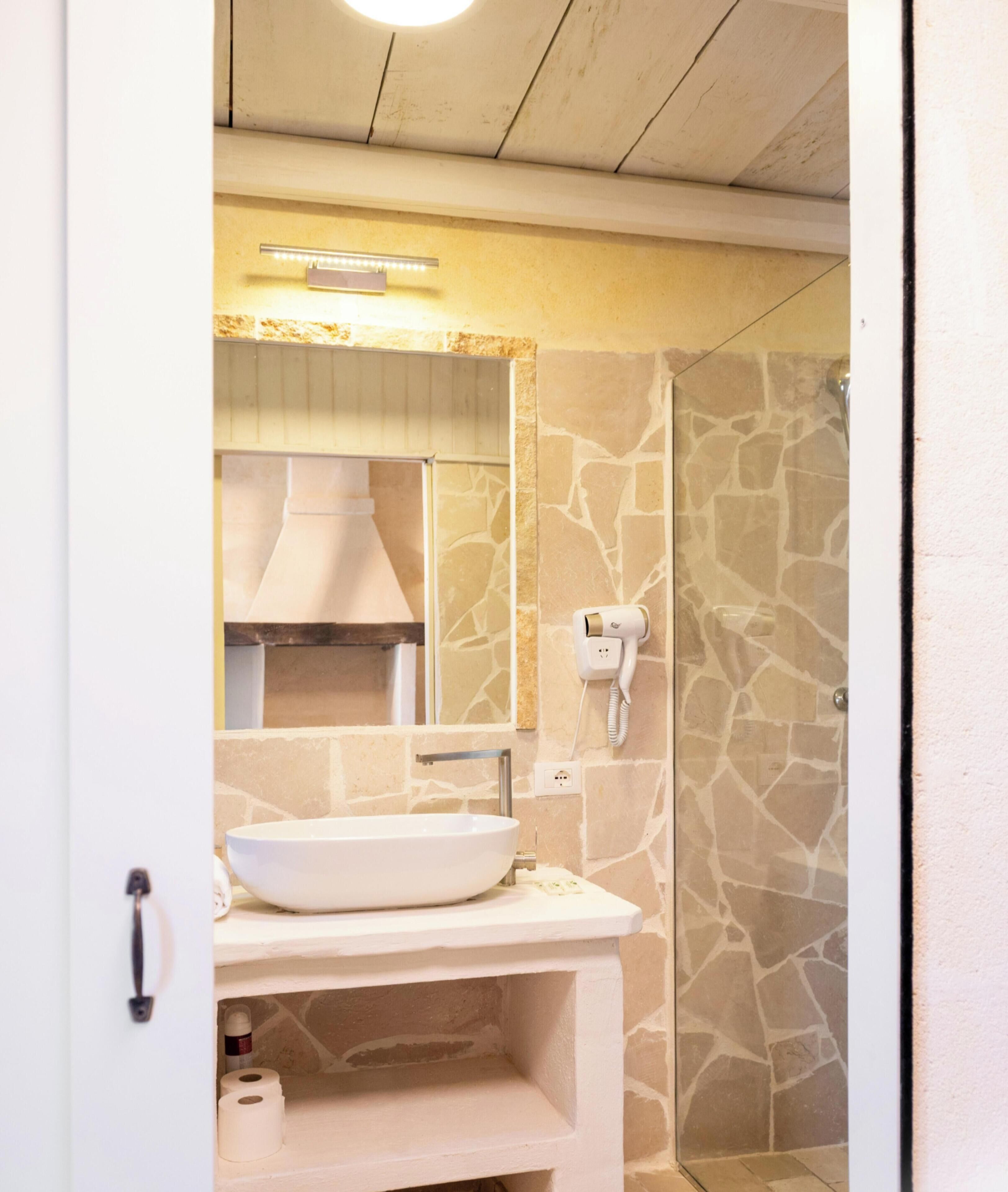 A bathroom with a stone wall, a white sink, a mirror, and a shower area.