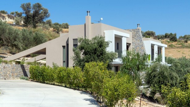 A modern two-story house with a stone chimney, large windows, and a sloped roof. - Anthemis Luxury Villas 2 (Heraklion)