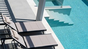 A pool area with lounge chairs and a clear blue pool. - Anthemis Luxury Villas 2 (Heraklion)