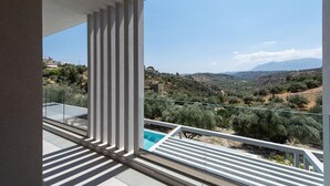 A balcony with a pool, overlooking a hilly landscape with olive trees and distant mountains. - Anthemis Luxury Villas 2 (Heraklion)