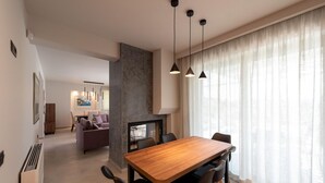 A modern dining area with a wooden table and black chairs, a stone accent wall, and a large window with sheer curtains. - Anthemis Luxury Villas 2 (Heraklion)
