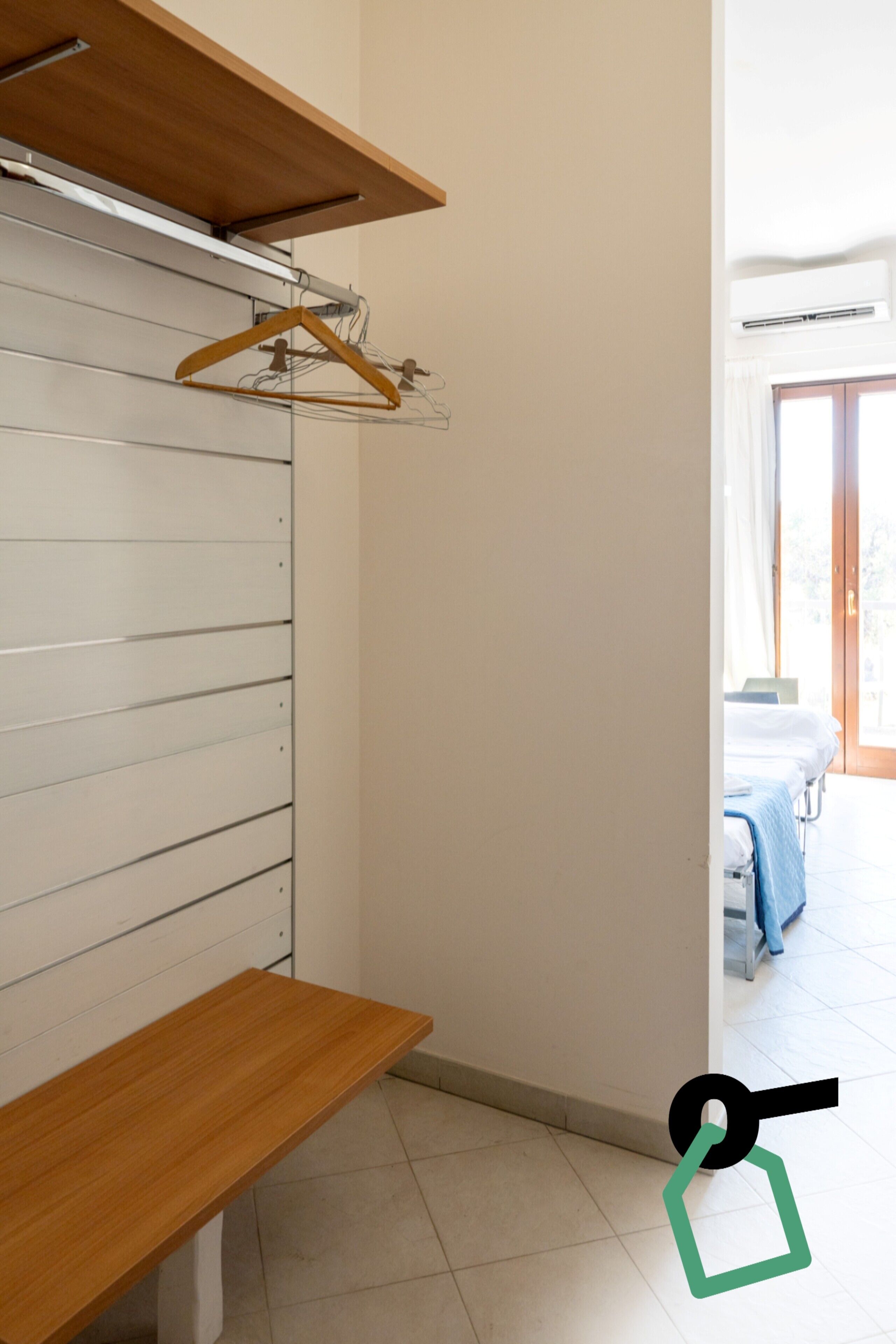 A room with a wooden bench, a hanging coat rack, and a bed with a blue blanket.