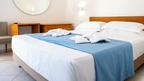 A hotel room with a bed, a round mirror, a nightstand, a desk, and a wall-mounted light.