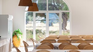 A dining area with tables and chairs, a large window with a view of trees, and a potted plant.