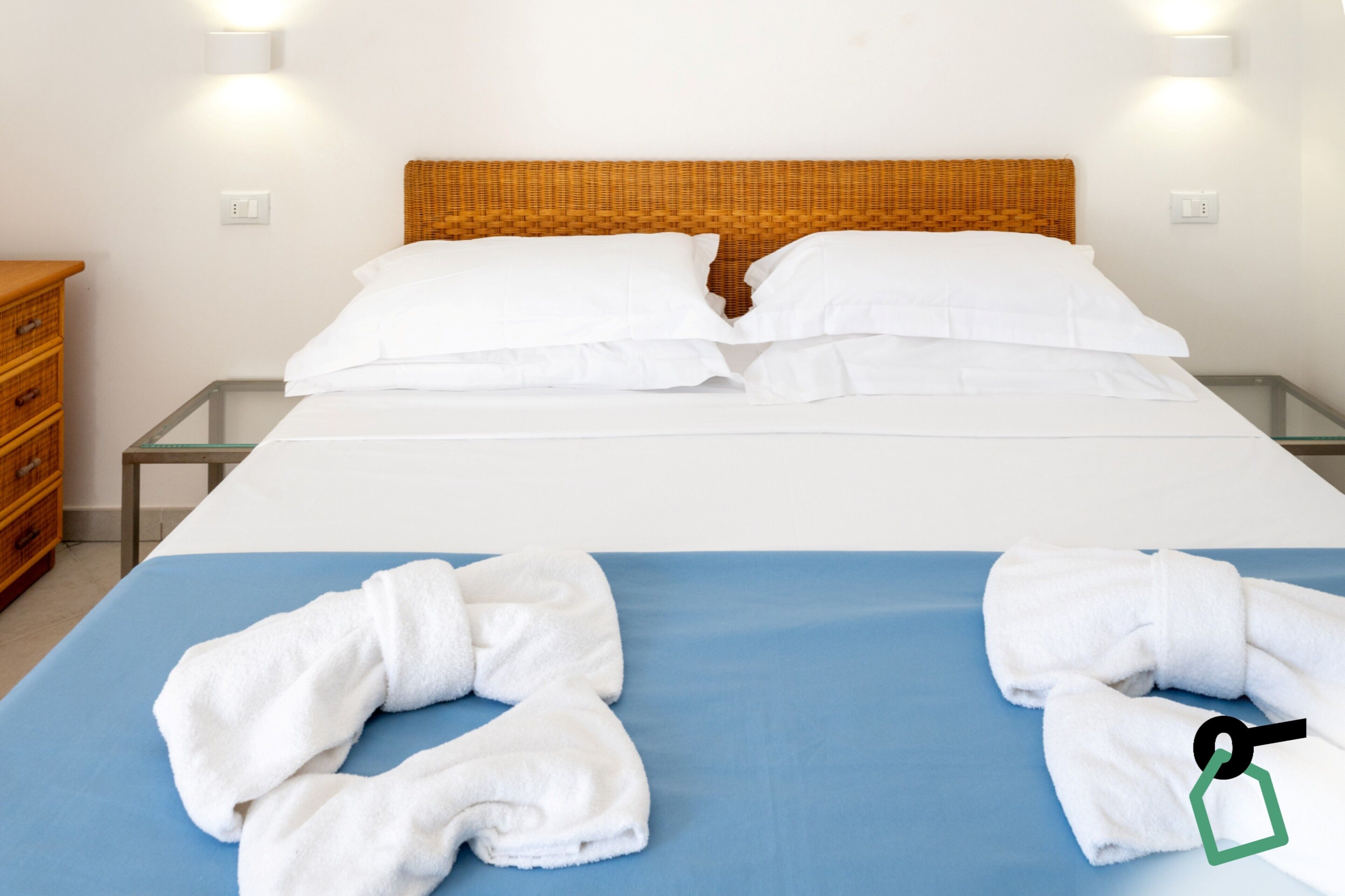 Une chambre d’hôtel avec un lit, un matelas bleu, des oreillers blancs, une tête de lit en bois et une table de chevet en bois avec une lampe.