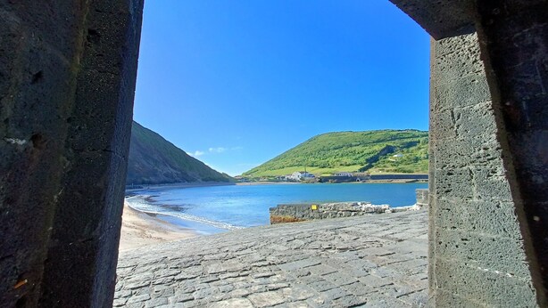Un arco in pietra che conduce a una spiaggia, con vista libera sul mare e una collina verde in lontananza.