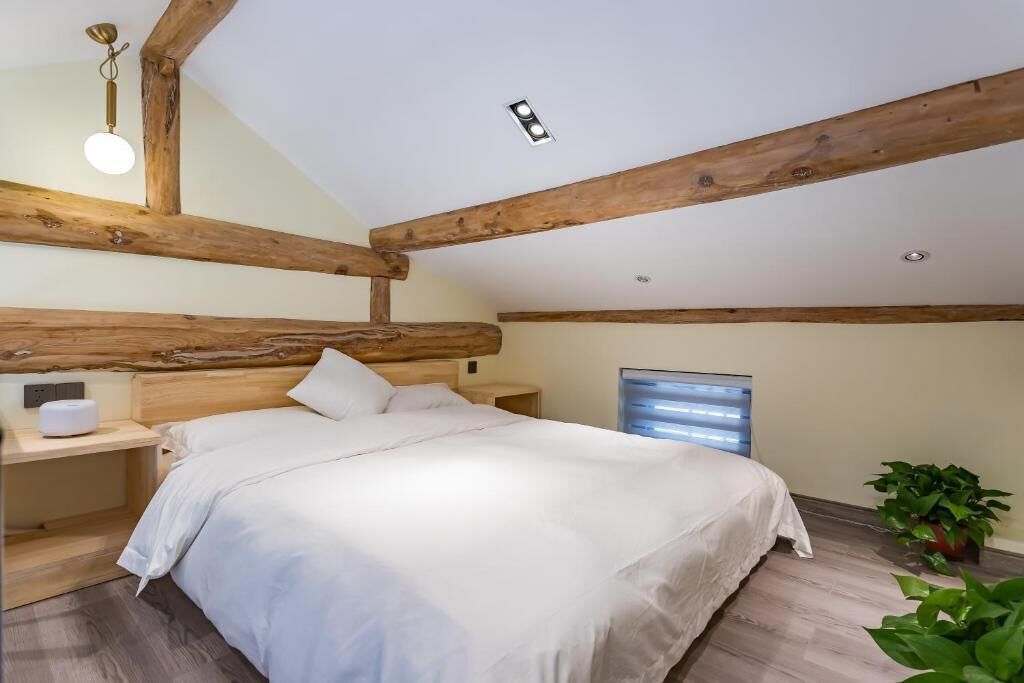 A bedroom with a wooden ceiling, a bed with white bedding, a bedside table, and a window with blinds.