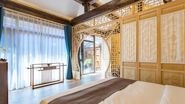A hotel room with a large bed, a balcony with a railing, and a decorative wooden screen. - Templeside Courtyard Hotel  (Beijing)