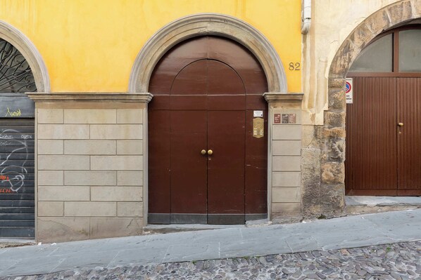 A brown double door with a keypad lock, set within a yellow building with stone walls and a brick base.