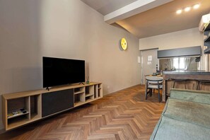 A modern living room with a flat-screen TV on a wooden console, a herringbone-patterned wooden floor, and a kitchen area with a bar counter and stools. - Appartamento Smeraldo - Immobili e Soluzioni Rent (Bergamo)