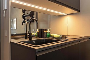 A modern kitchen with a stainless steel sink, a black faucet, and a mirror above the countertop. - Appartamento Smeraldo - Immobili e Soluzioni Rent (Bergamo)