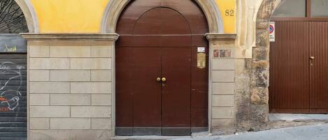 A brown double door with a keypad lock, set within a yellow building with stone walls and a brick base.
