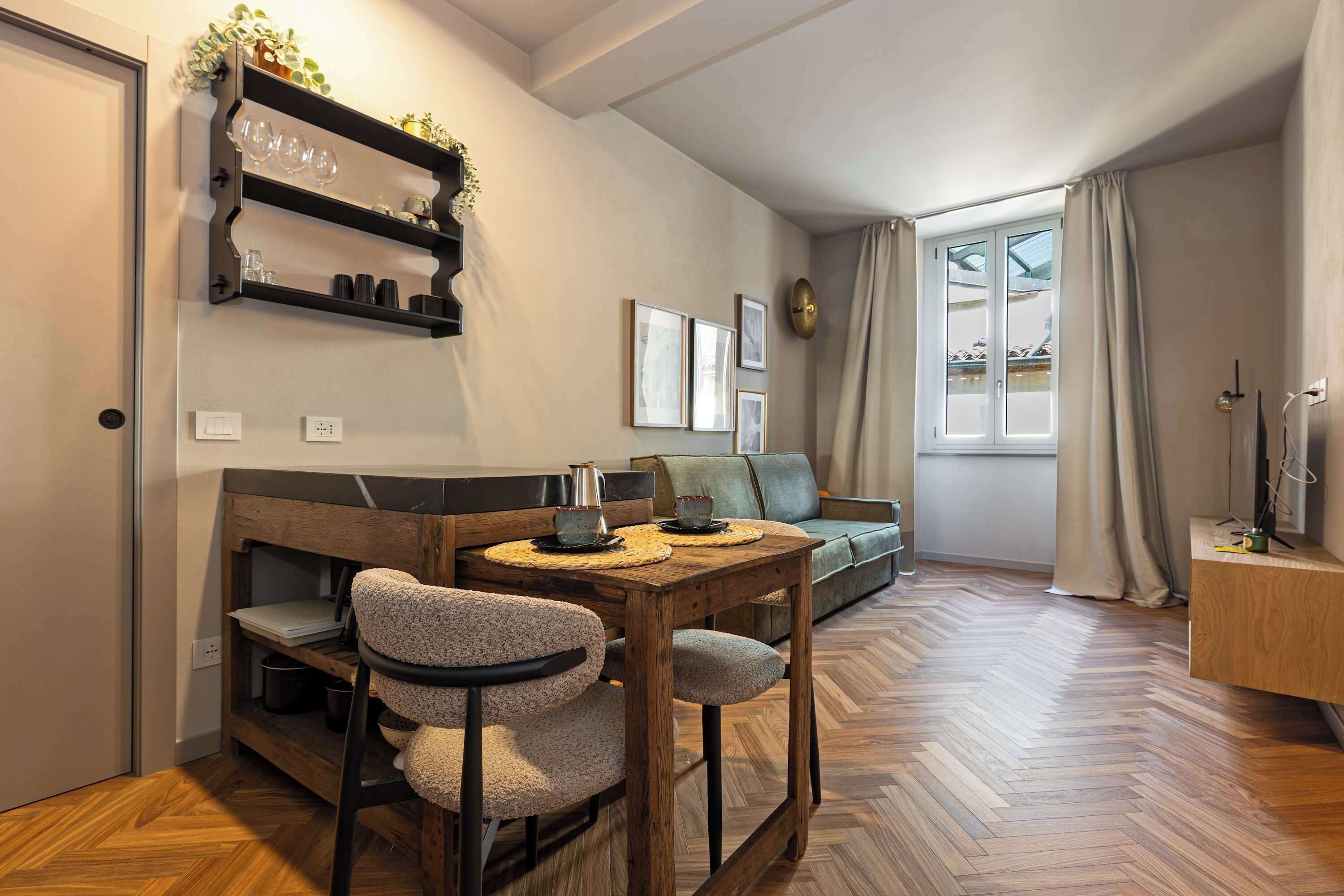 A cozy living area with a wooden dining table, two chairs, a sofa, and a window with curtains.