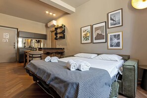 Hotellihuone, jossa on sänky, työpöytä, tuoli ja pieni keittiönurkkaus.