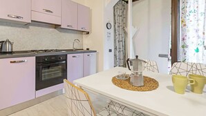 Une cuisine équipée d’une cuisinière, d’un four et de placards, une table à manger avec des chaises, et une fenêtre avec des rideaux.