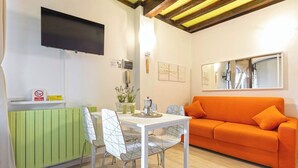 Un salon moderne avec une table blanche, deux chaises, un canapé orange, un téléviseur à écran plat et un radiateur vert.