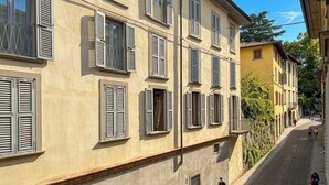 Un immeuble à plusieurs étages avec des fenêtres fermées par des volets et une rue étroite.