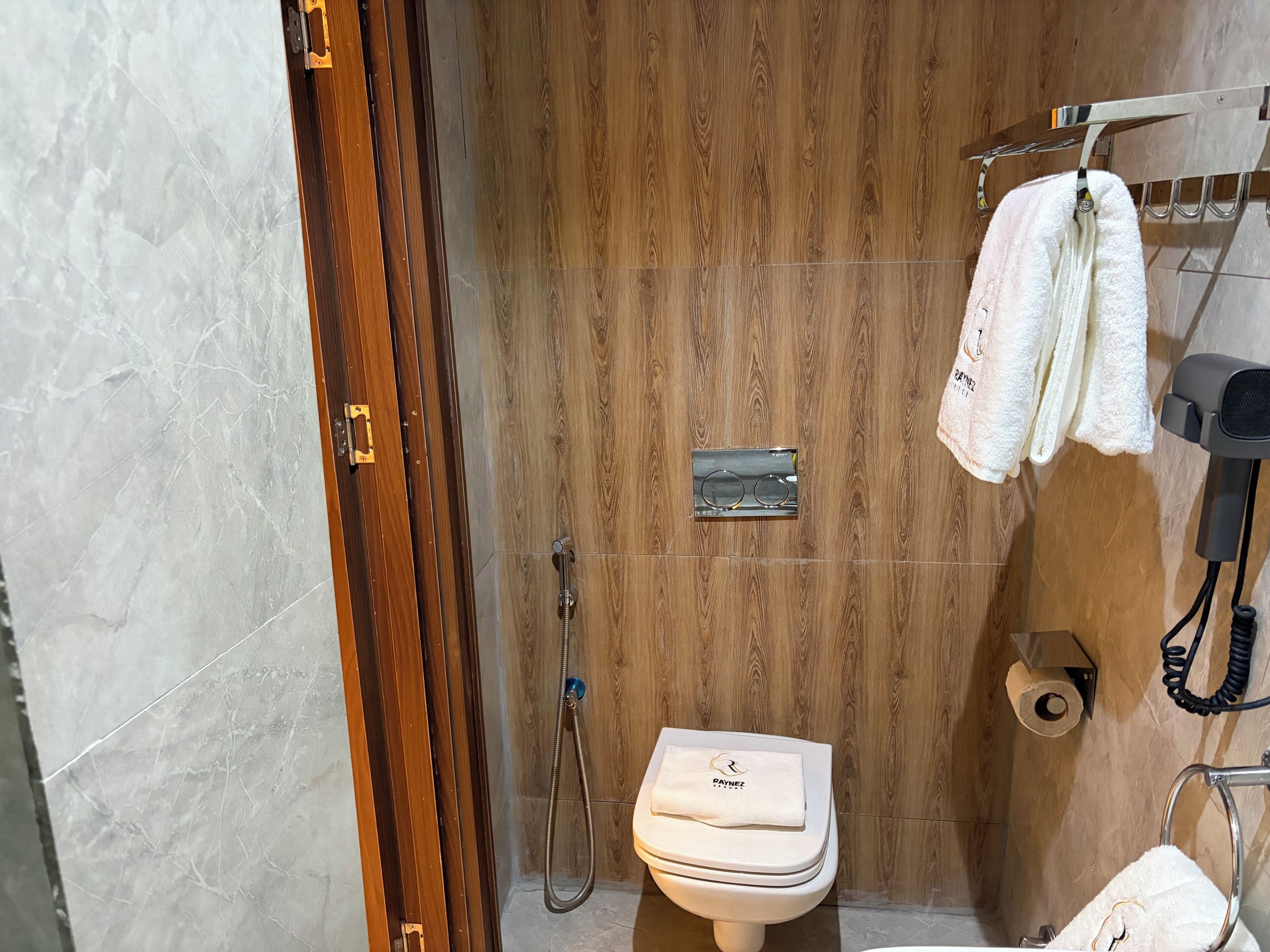 A bathroom with a wooden vanity, a toilet, a shower, and a hairdryer.