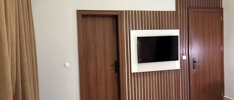 Ein Hotelzimmer mit Holzschrank, Wandfernseher, kleinem runden Tisch und rotem Sessel.