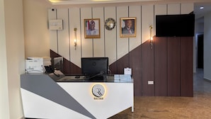 A reception desk with a logo, a computer, and a telephone. There are framed pictures and a clock on the wall. - Raynez Resort (Abuja)