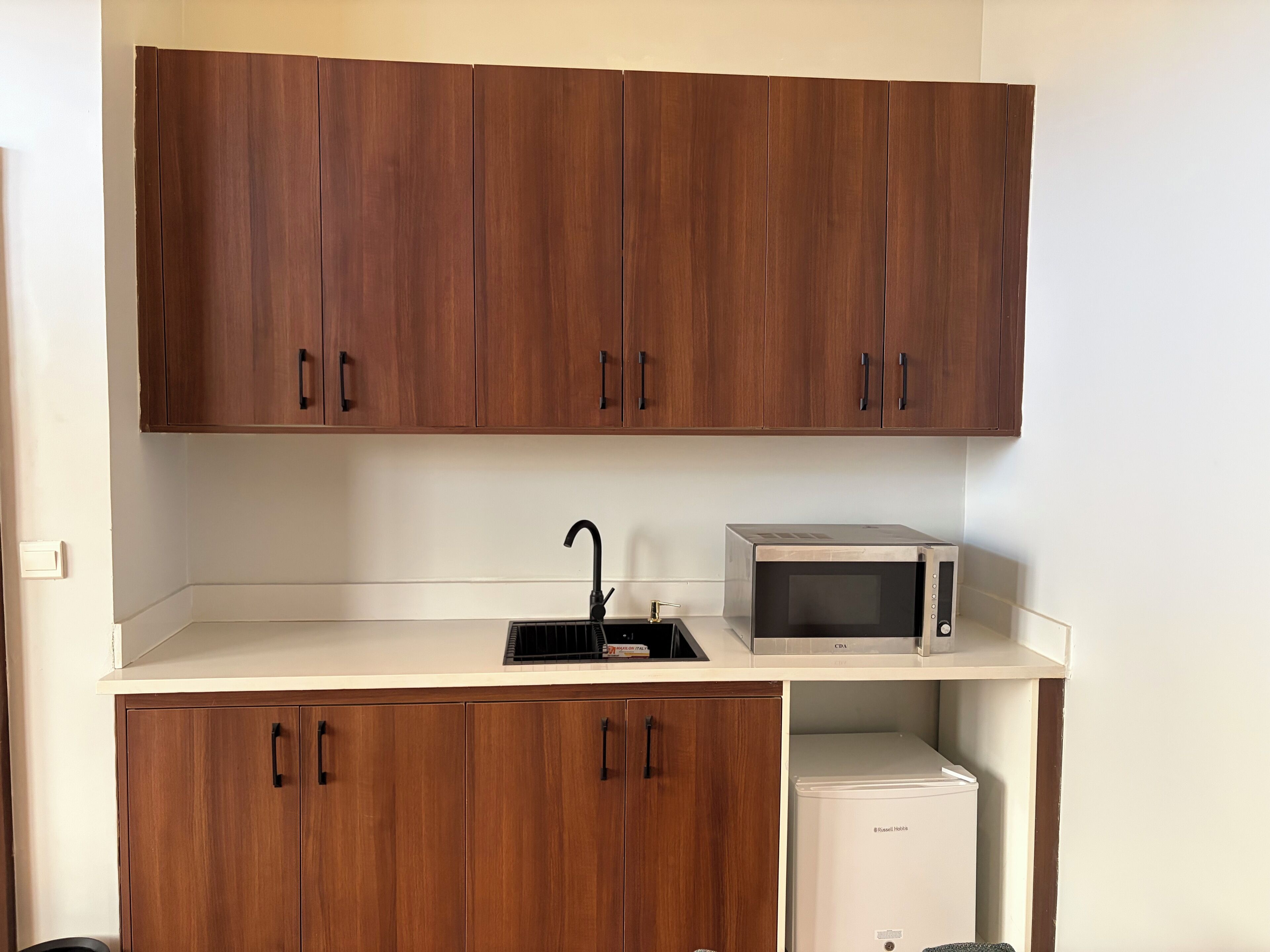 A compact kitchen with wooden cabinets, a sink, a microwave, and a mini refrigerator.