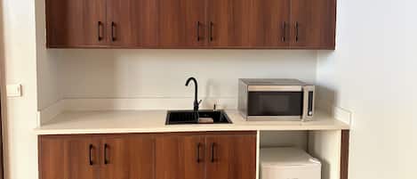 A compact kitchen with wooden cabinets, a sink, a microwave, and a mini refrigerator.