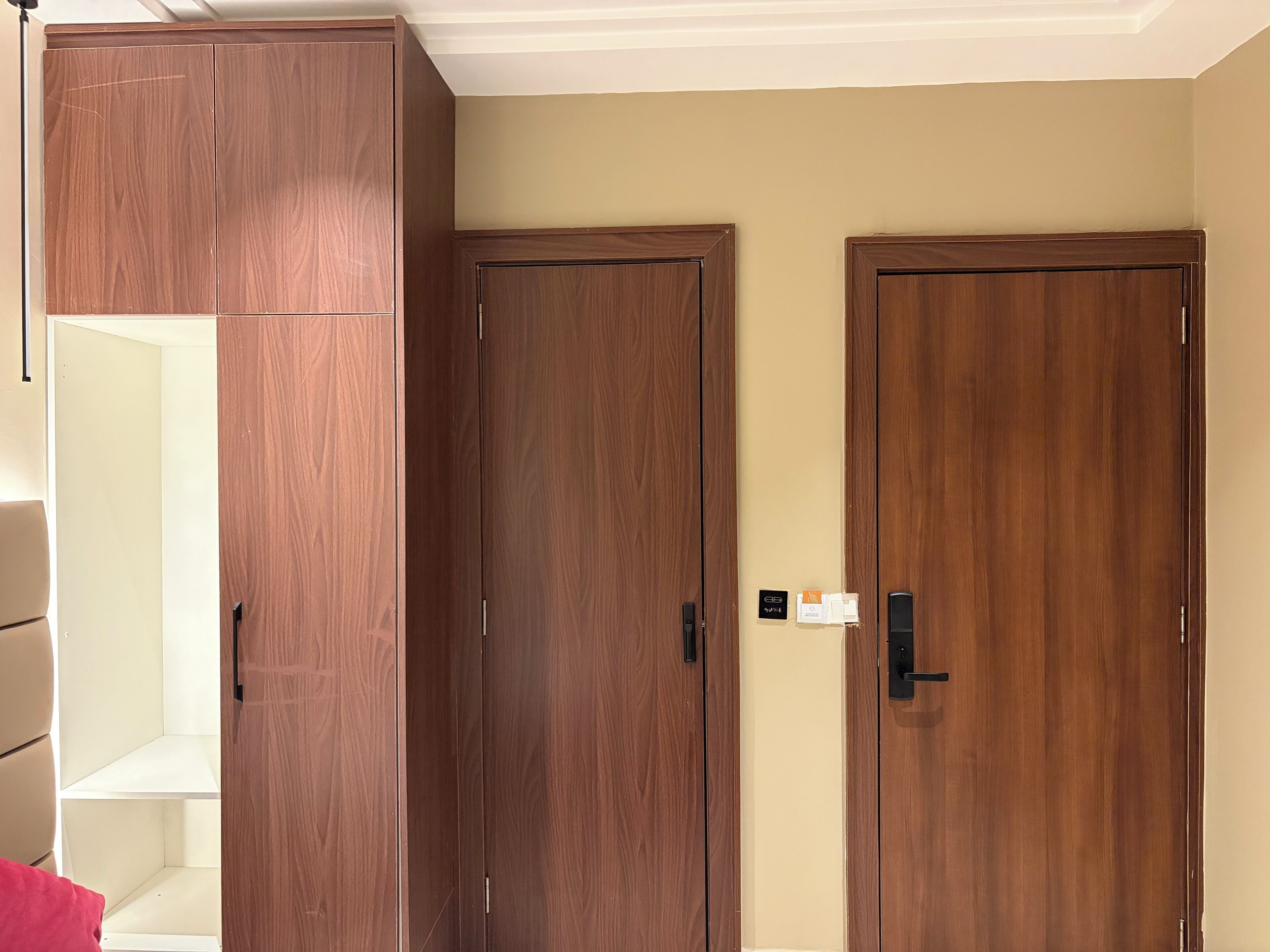 A room with a large wardrobe, two closed doors, and a light switch on the wall.