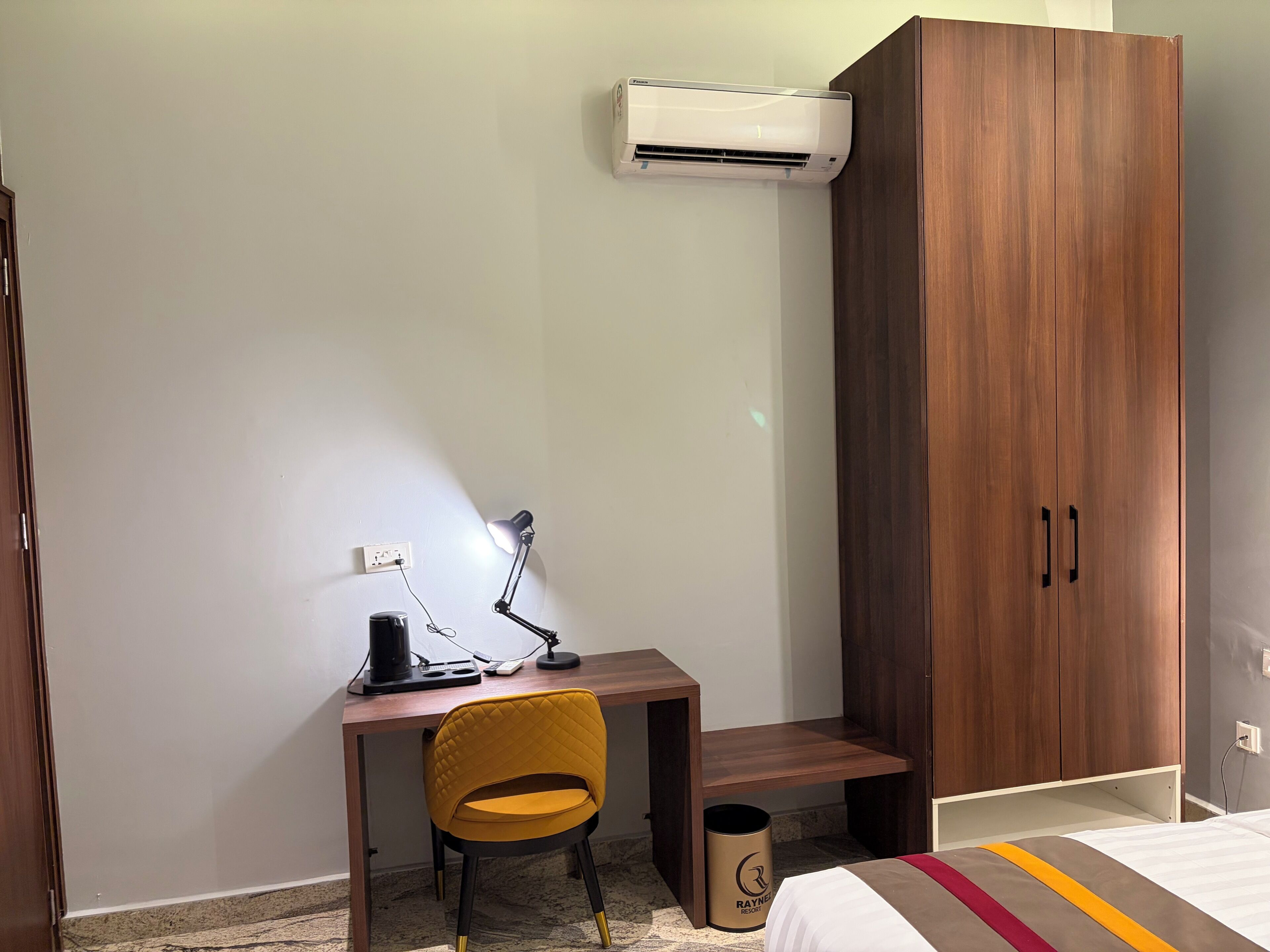 A bedroom with a bed, a desk with a chair, an air conditioner, and a wardrobe.