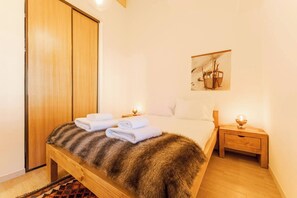 Ein Schlafzimmer mit einem hölzernen Bett, einem Fellüberwurf, zwei weißen Handtüchern, einem Nachttisch mit Lampe und einem Bild an der Wand.