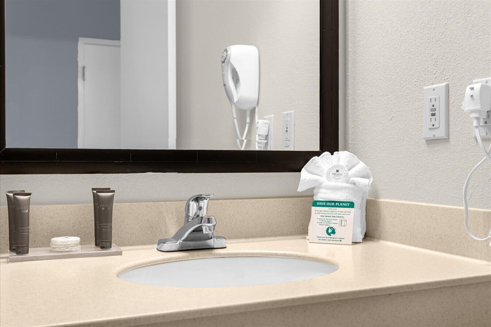 Une salle de bain équipée d’un lavabo, d’un miroir, d’un sèche-cheveux et d’articles de toilette.