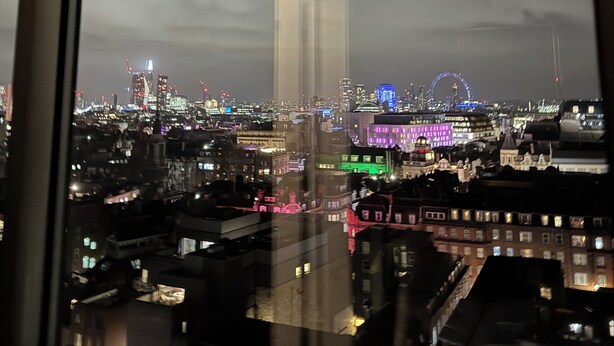 A nighttime cityscape through a window, featuring illuminated buildings and a Ferris wheel. - Soho 360 Views Flat (London)