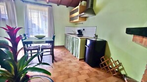 Une cuisine de taille réduite comprenant une table à manger, des chaises, un réfrigérateur et une fenêtre avec des rideaux.