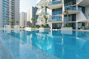 Um hotel moderno com piscina, rodeado por arranha-céus e palmeiras.