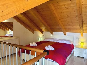 Ein Schlafzimmer mit Holzboden, einem Bett mit rot-weißer Bettwäsche, einem Nachttisch mit Lampe und einer weißen Kommode.