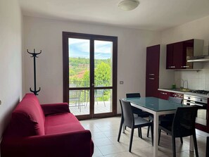 A modern kitchen with a dining table, chairs, and a red sofa. - App.12- Le Terrazze del Garda Immobili e Soluzioni (Manerba del Garda)