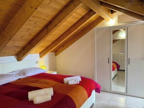 A bedroom with a wooden ceiling, a bed with a red and orange bedspread, white pillows, and a white wardrobe. - App.12- Le Terrazze del Garda Immobili e Soluzioni (Manerba del Garda)