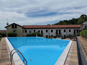 Ein Schwimmbecken mit Fliesen, ein Gebäude mit rotem Ziegeldach und ein klarer Himmel.